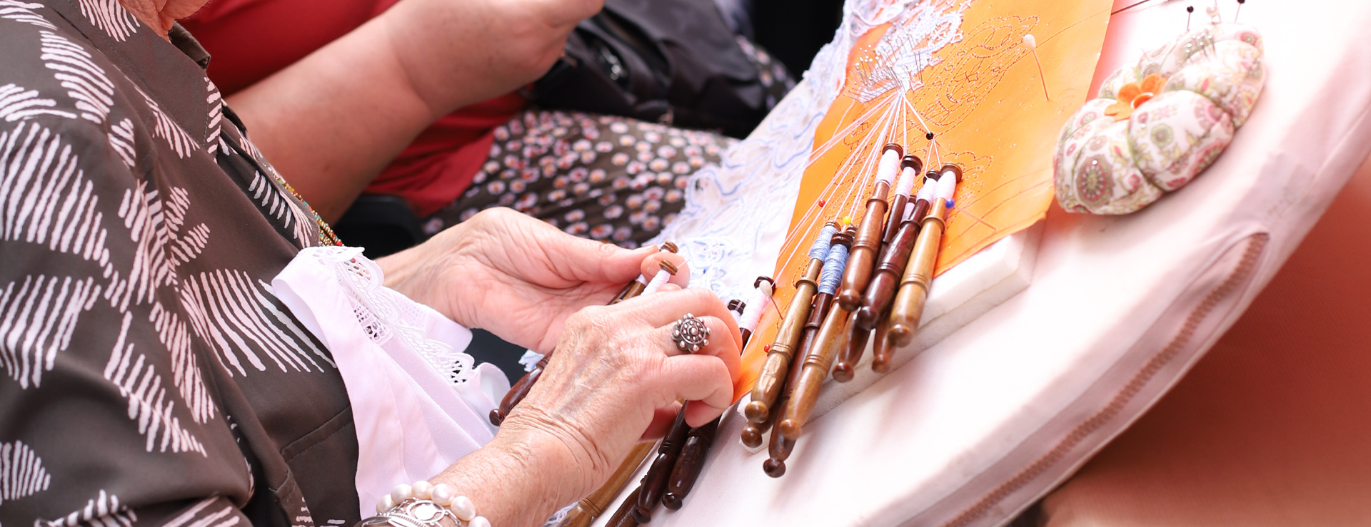 Mans d’una artesana fent puntes de coixí amb boixets